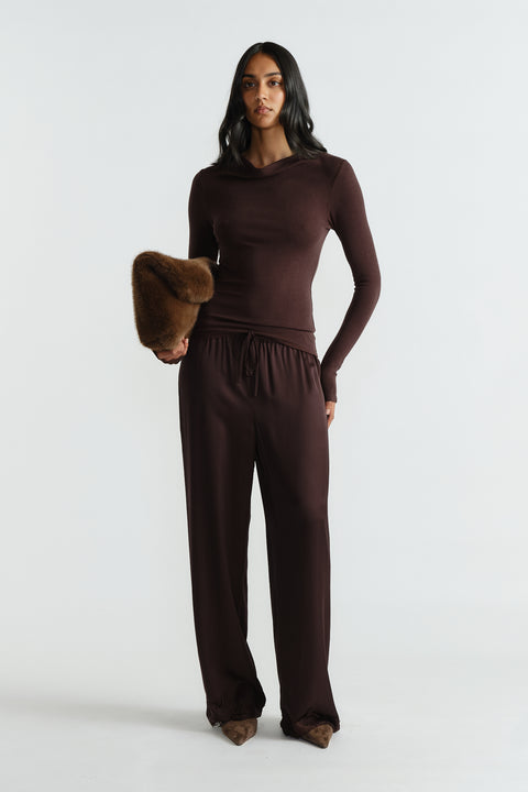Woman wearing a rich mocha long sleeve top paired with matching relaxed pants and holding a brown fur clutch.