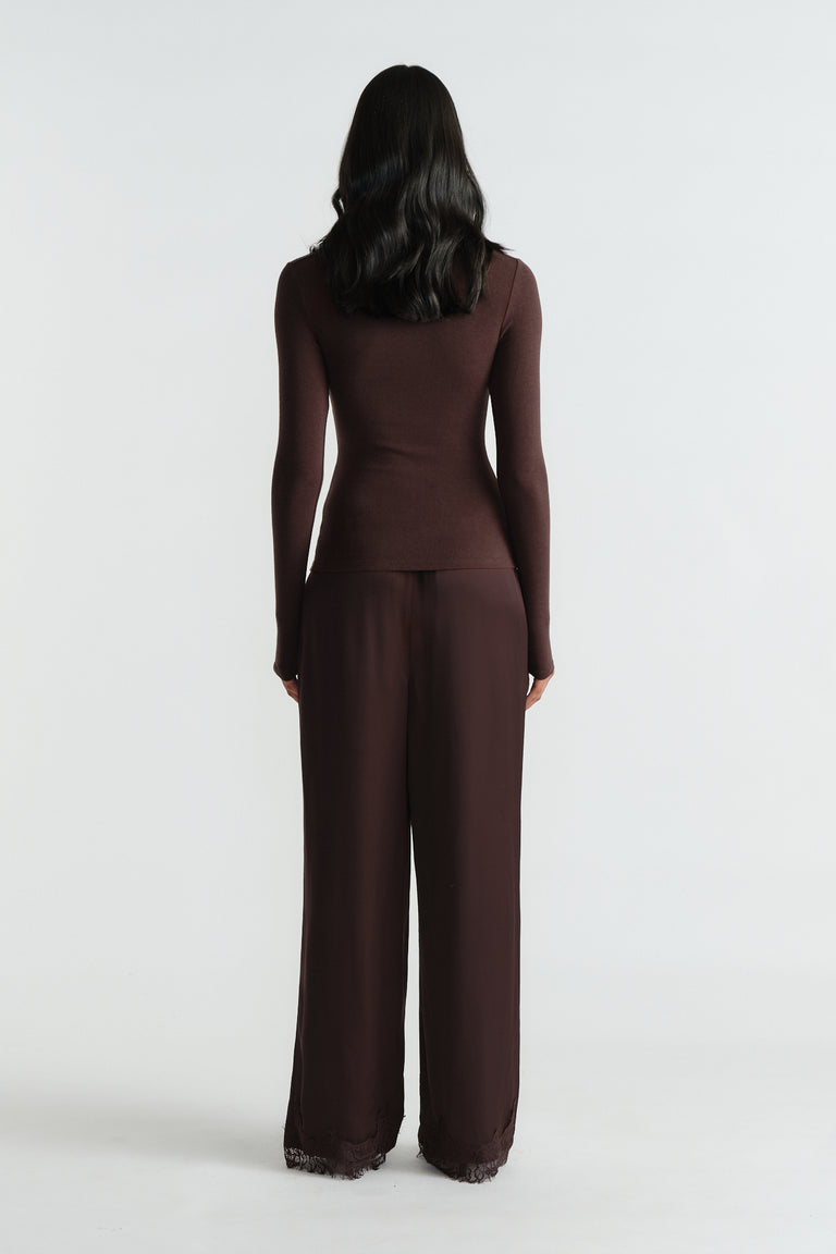 Woman wearing a fitted long sleeve top paired with loose wide-leg pants featuring lace trim at the hem, back view.