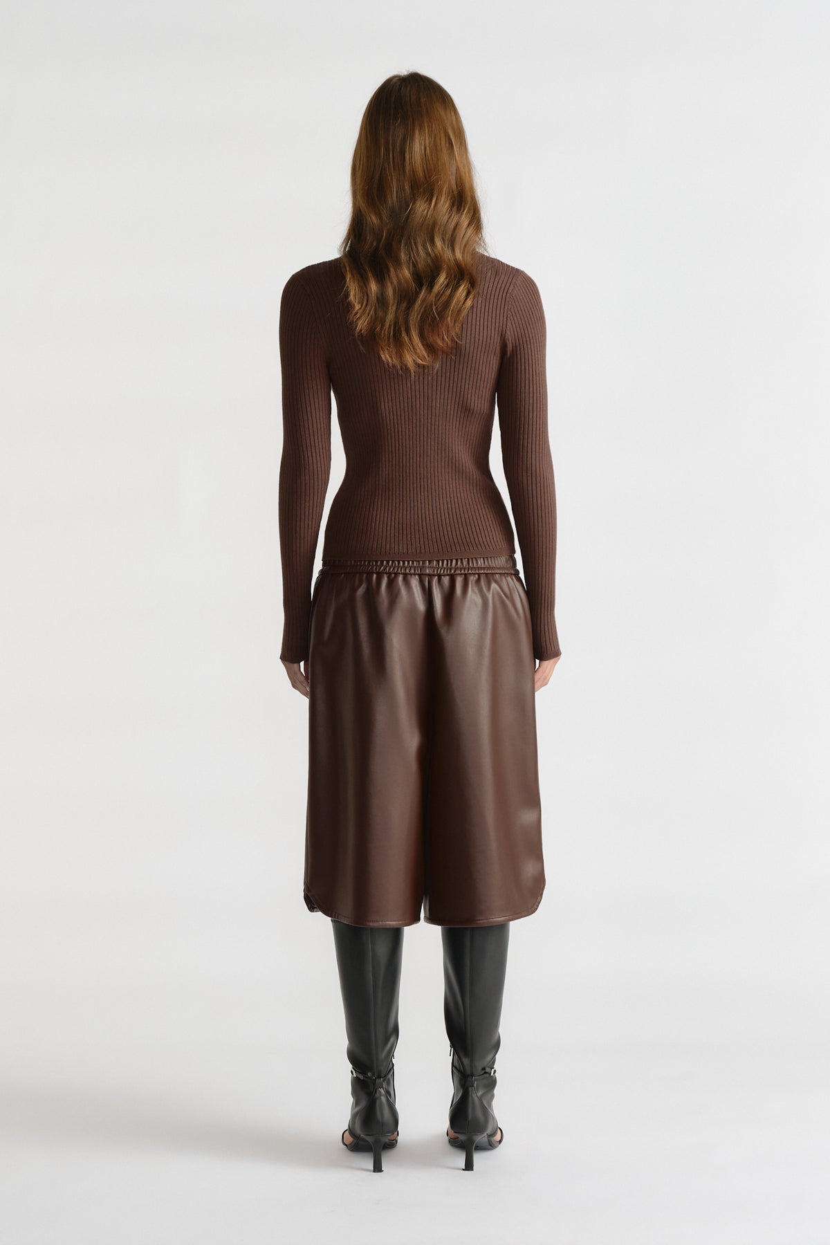 Back view of D-Luxe Knit Zip Long Sleeve in warm walnut brown with textured rib knit, styled with leather culottes and black boots.