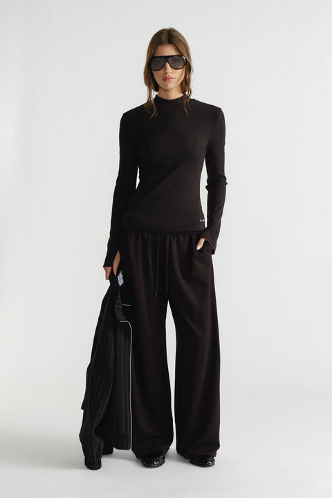 Woman wearing a sleek black ribbed long-sleeve top paired with loose wide-leg pants and oversized sunglasses