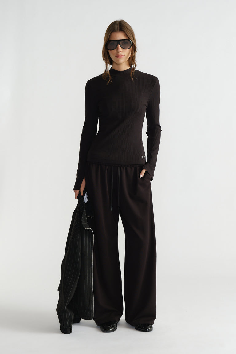 Woman wearing a sleek black ribbed long-sleeve top paired with loose wide-leg pants and oversized sunglasses
