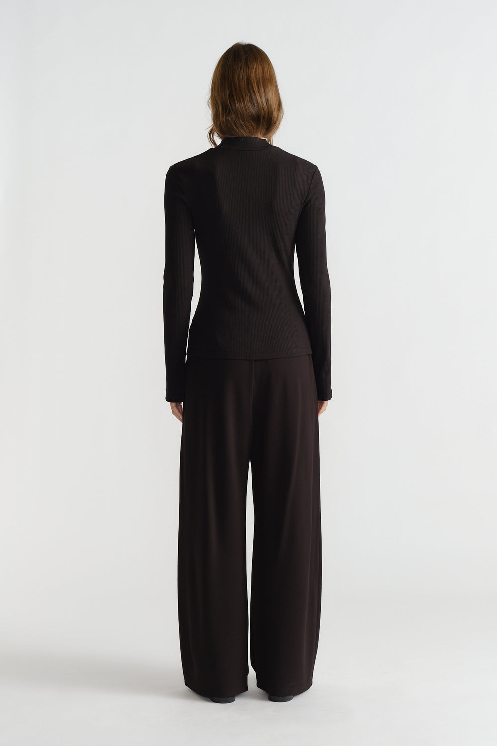 Back view of woman wearing a fitted long-sleeve black ribbed top paired with loose wide-leg pants for a sleek look