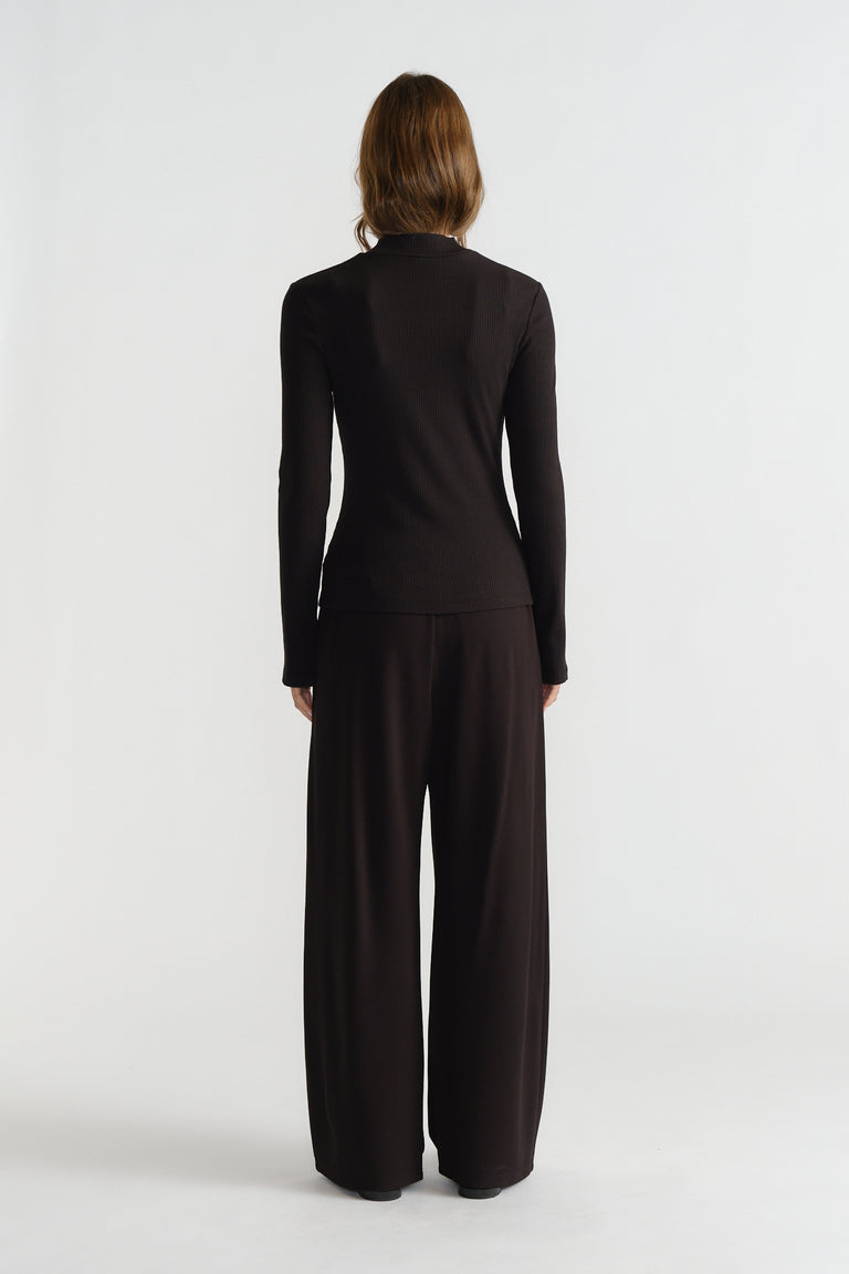 Back view of woman wearing a fitted long-sleeve black ribbed top paired with loose wide-leg pants for a sleek look