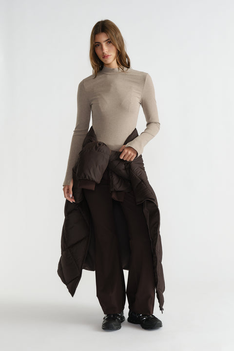 Woman wearing a fitted long sleeve ribbed top in a neutral tone paired with dark wide-leg pants and black sneakers
