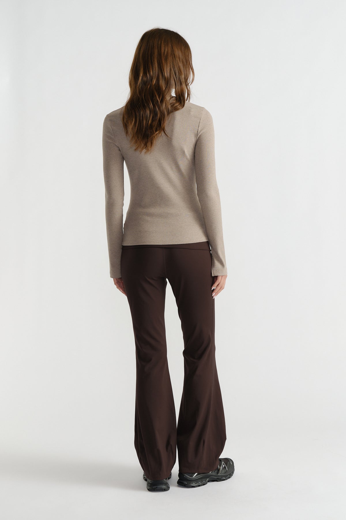 Back view of woman wearing a fitted beige ribbed long sleeve top with dark brown flared pants and black shoes