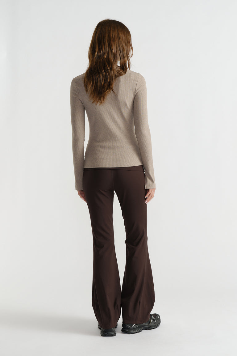 Back view of woman wearing a fitted beige ribbed long sleeve top with dark brown flared pants and black shoes