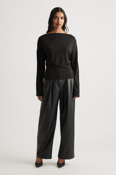 Woman wearing a fitted black long sleeve top with cinched waist paired with wide-leg leather-look pants and heels