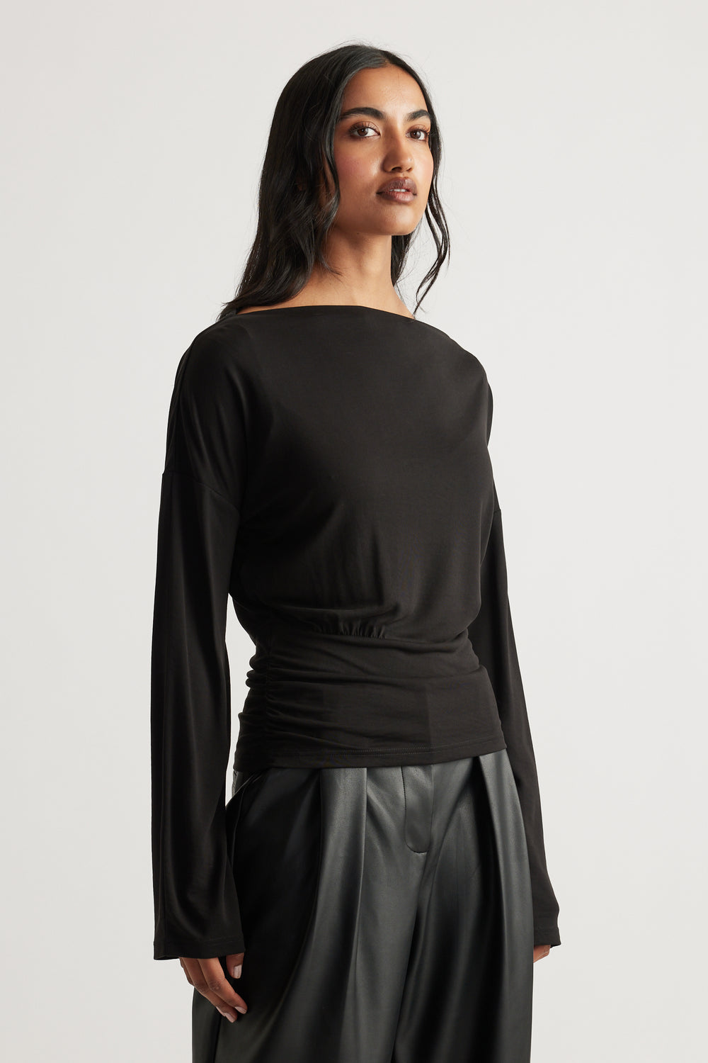 Woman in a fitted black long sleeve top with subtle cinching, paired with loose black leather-look pants for modern edge.