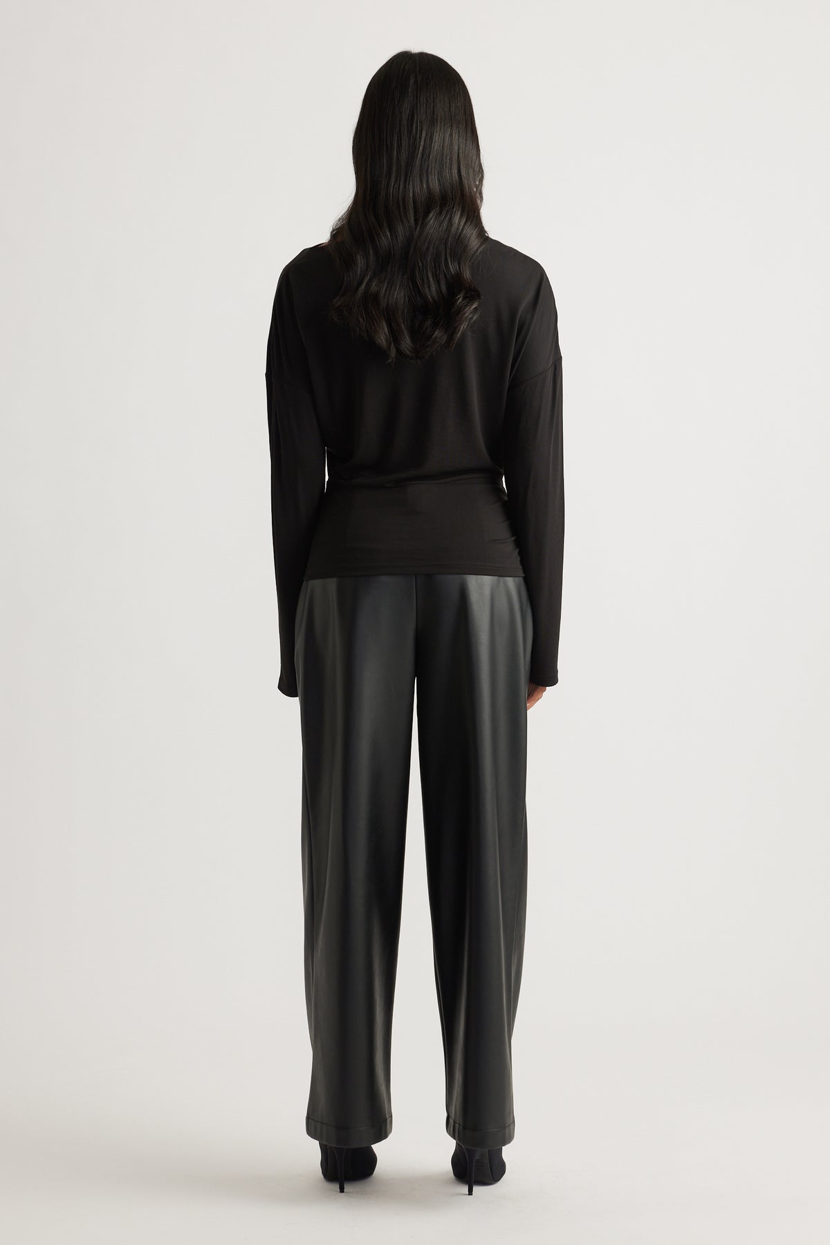 Woman wearing a fitted black long sleeve top with cinched waist, paired with loose black wide-leg trousers and heels.