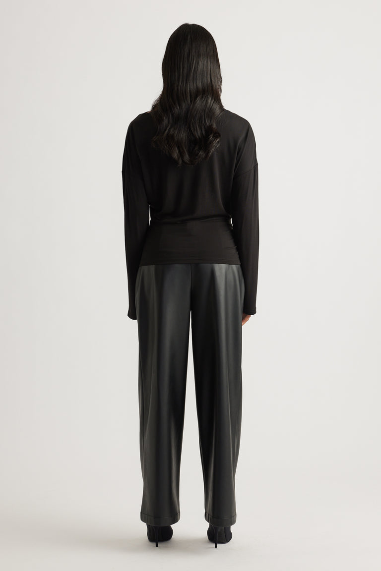 Woman wearing a fitted black long sleeve top with cinched waist, paired with loose black wide-leg trousers and heels.