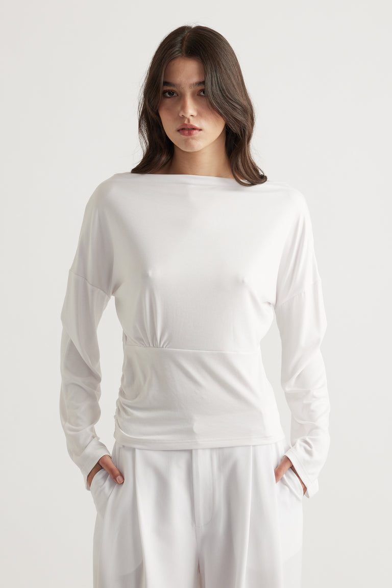 Woman wearing a white cinched long sleeve top with a relaxed fit paired with loose white pants for a minimalist look