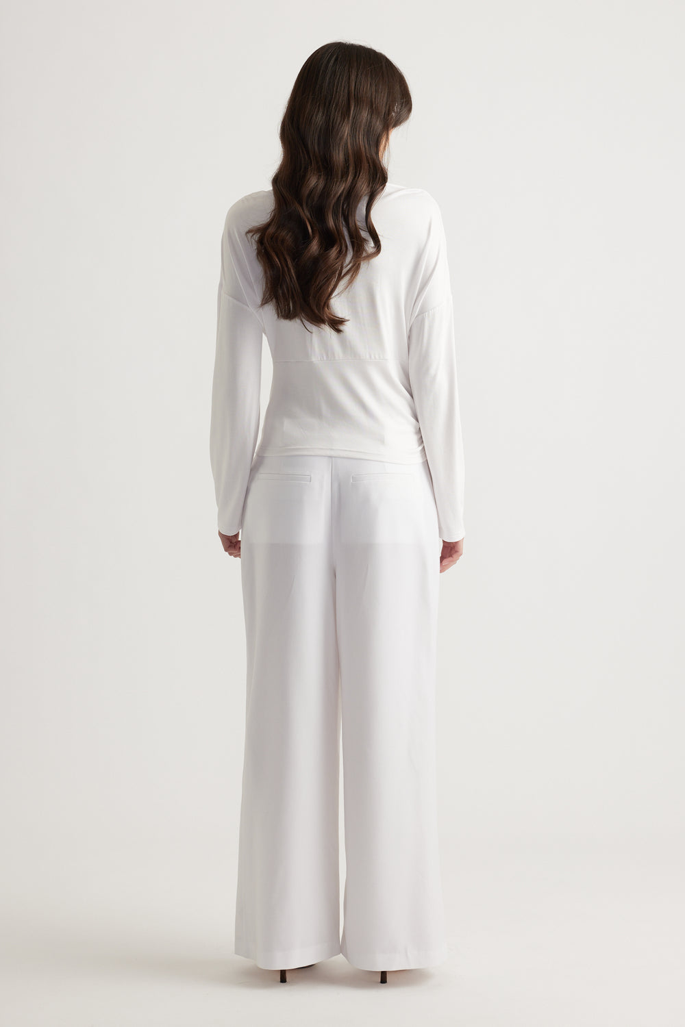 Woman seen from behind wearing a crisp white cinched long sleeve top paired with wide-leg white trousers for a sleek look