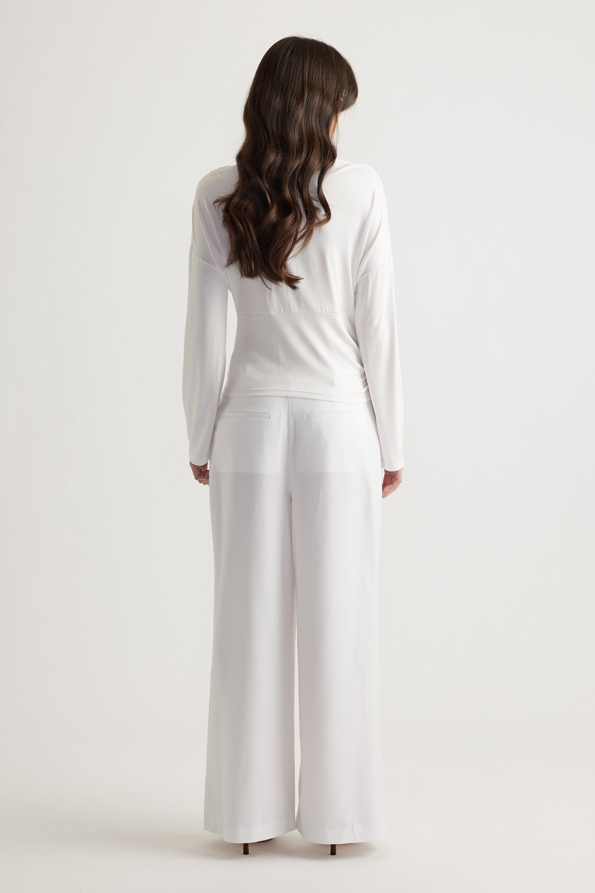 Woman seen from behind wearing a crisp white cinched long sleeve top paired with wide-leg white trousers for a sleek look