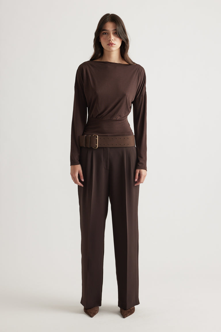 Woman wearing a fitted brown cinched long sleeve top with wide belt, paired with matching tailored trousers for a sleek look