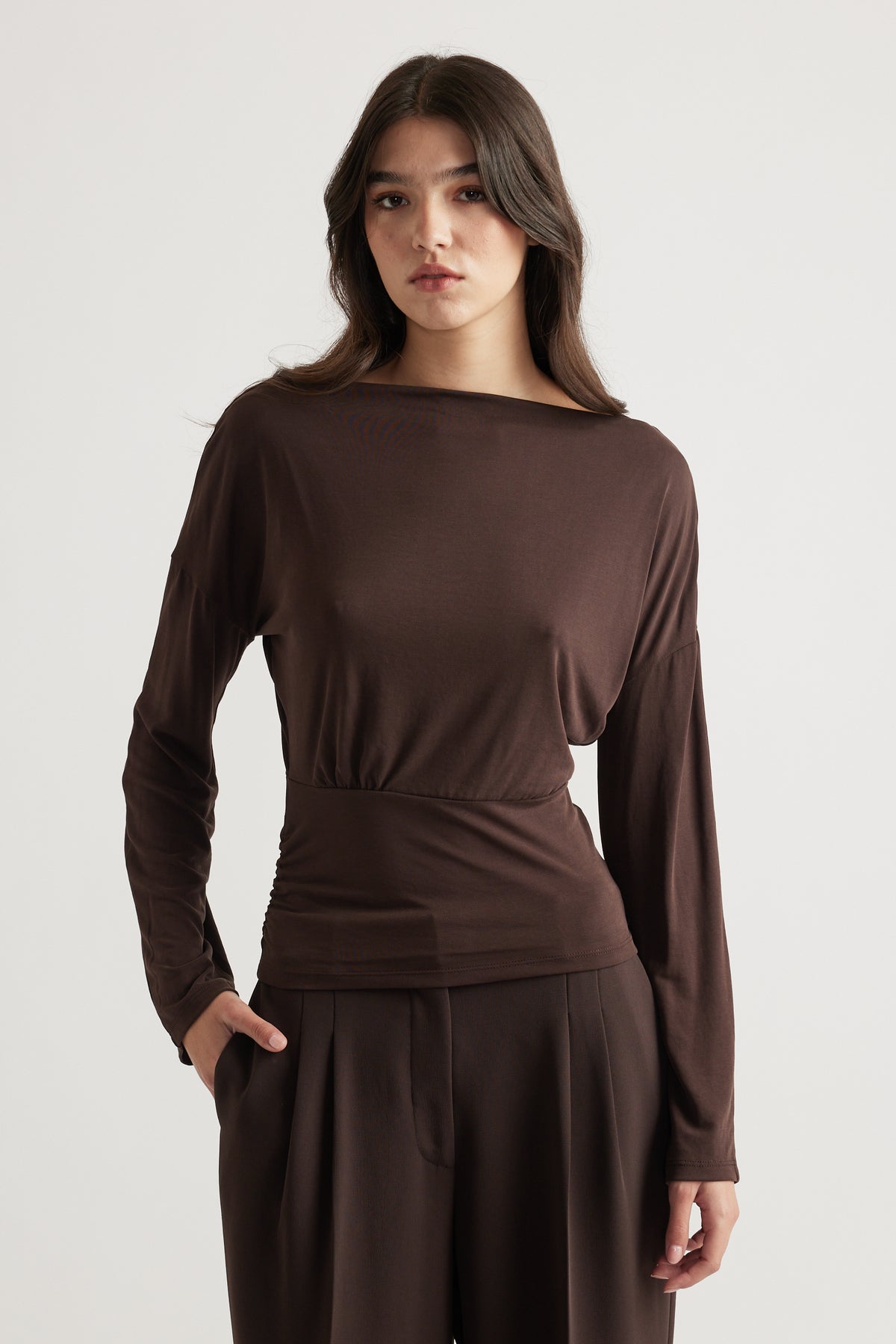 Woman wearing a sleek brown long sleeve top with cinched waist paired with loose tailored trousers for a refined look