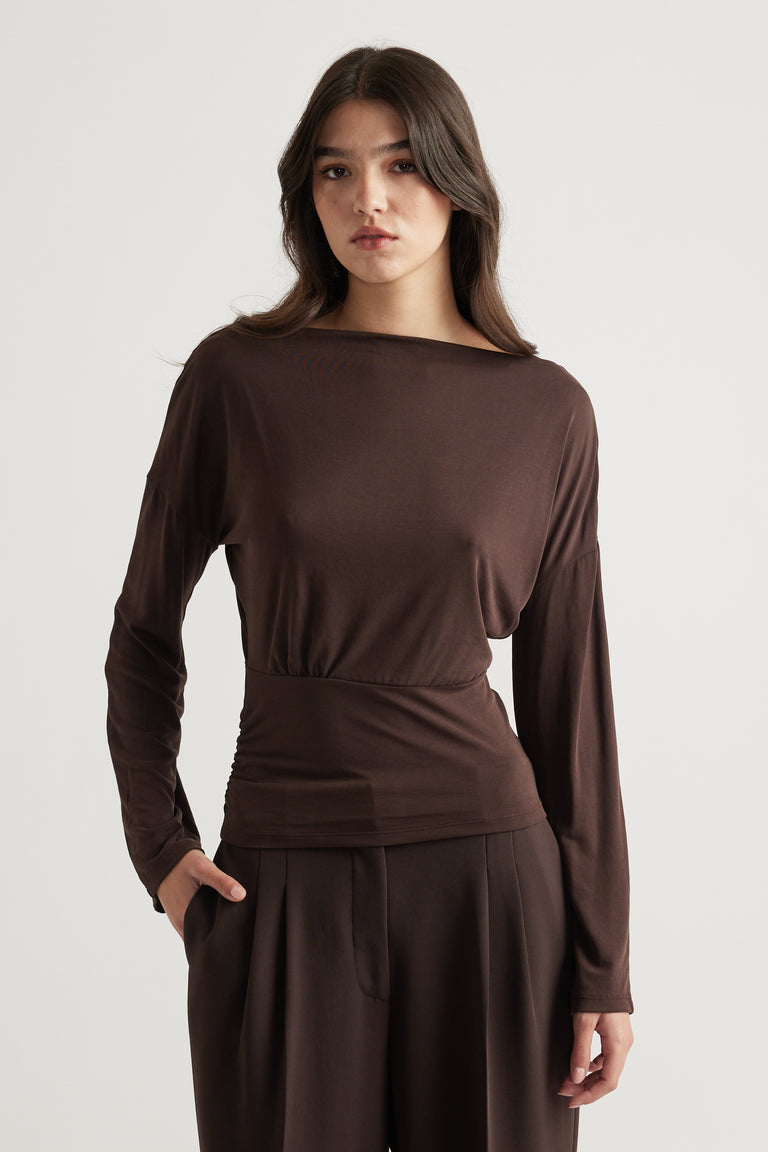 Woman wearing a sleek brown long sleeve top with cinched waist paired with loose tailored trousers for a refined look