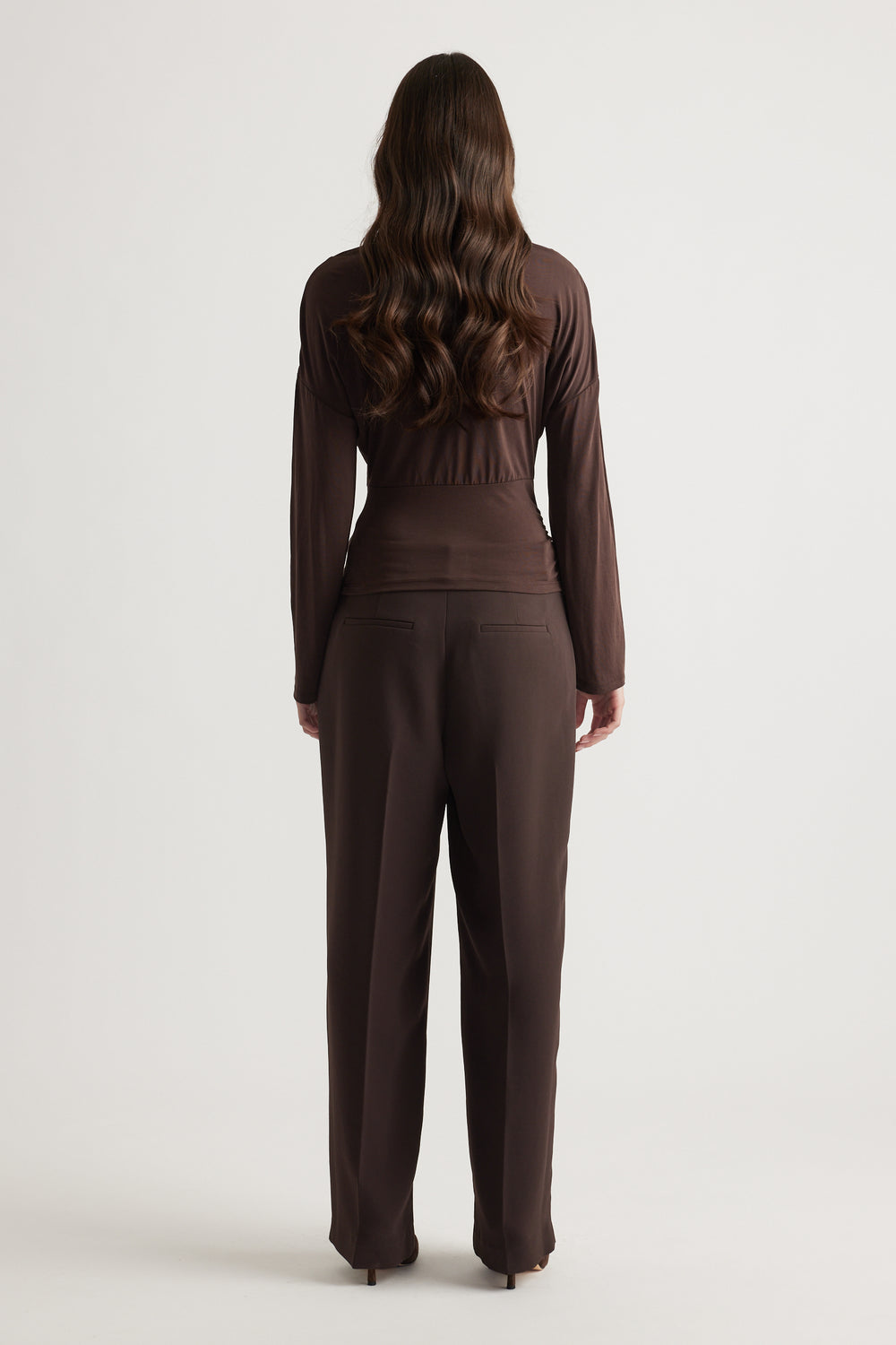 Woman wearing a fitted brown long sleeve top paired with matching tailored trousers for a sleek, polished look