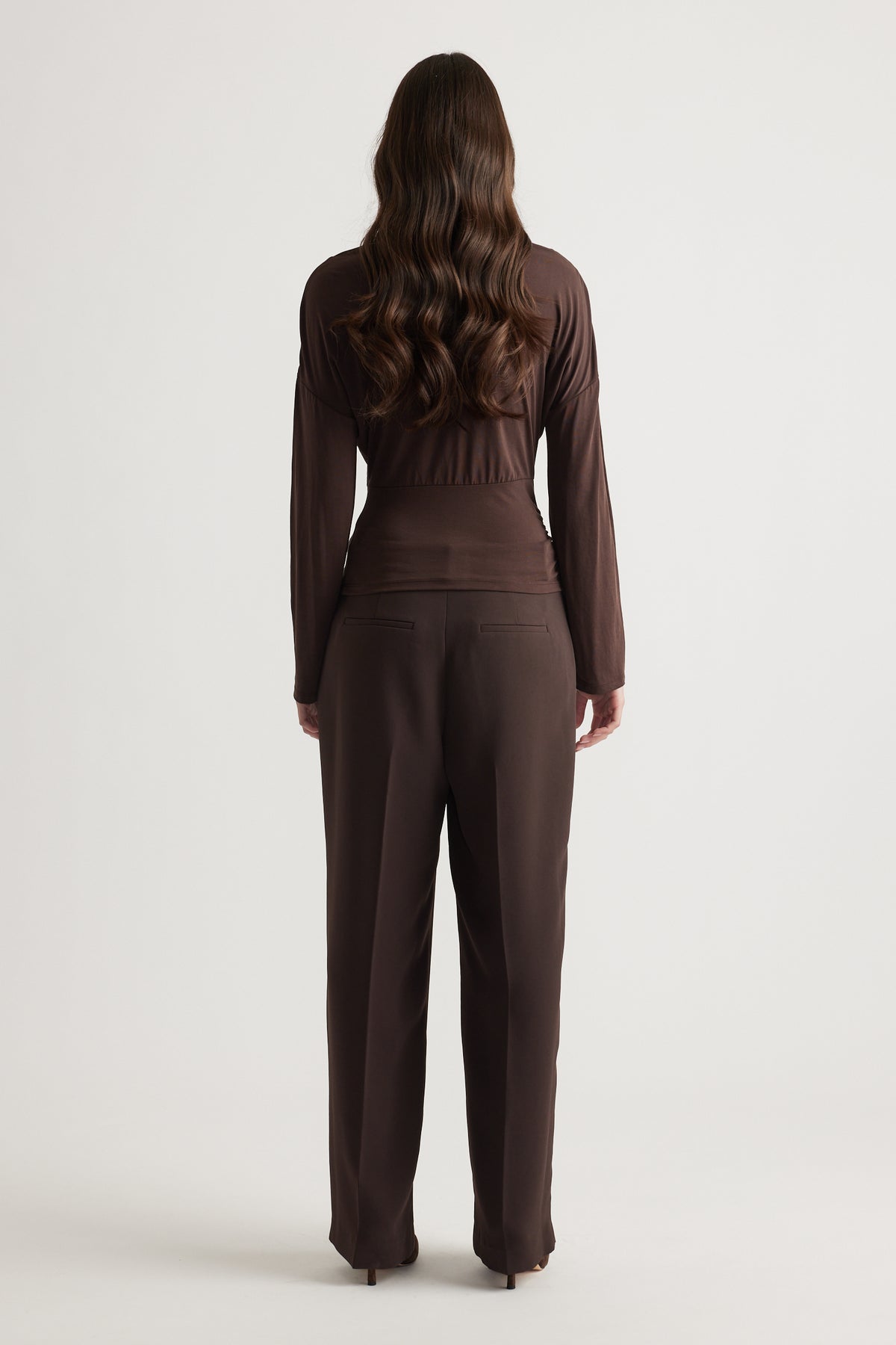 Woman wearing a fitted brown long sleeve top paired with matching tailored trousers for a sleek, polished look