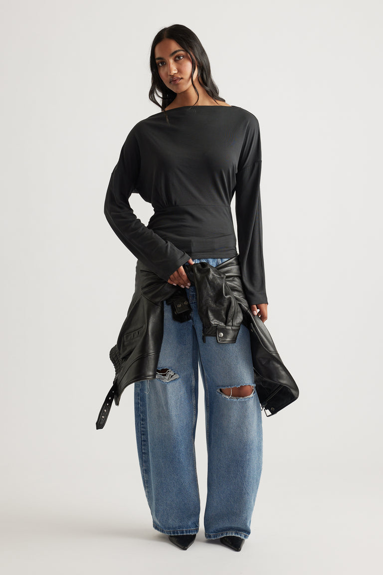 Woman wearing a fitted black long sleeve top paired with wide-leg distressed blue jeans and holding a leather jacket