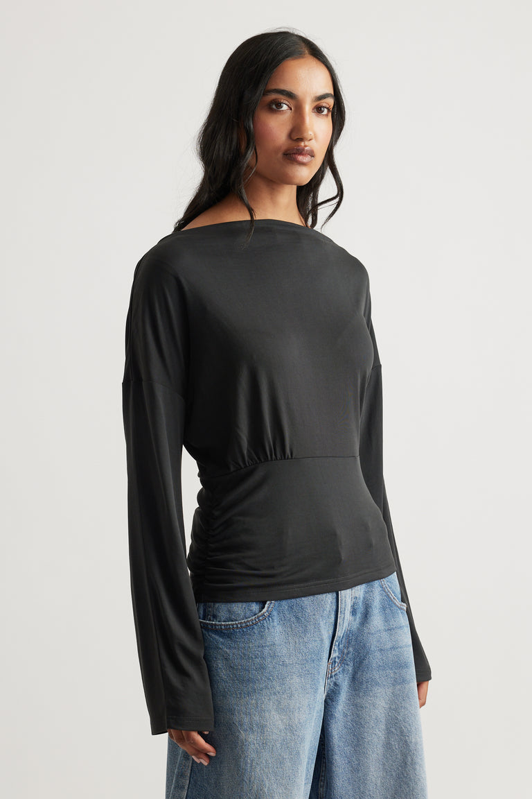 Woman wearing a charcoal long sleeve top with a cinched waist paired with relaxed light blue denim jeans