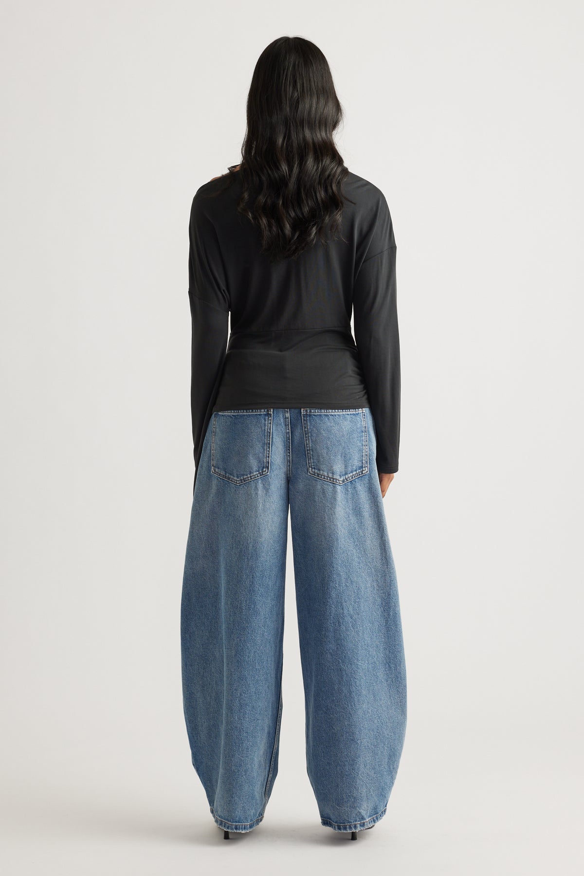 Woman shown from behind wearing a fitted black long sleeve top paired with wide-leg light blue denim jeans