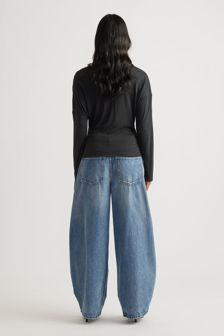 Woman shown from behind wearing a fitted black long sleeve top paired with wide-leg light blue denim jeans