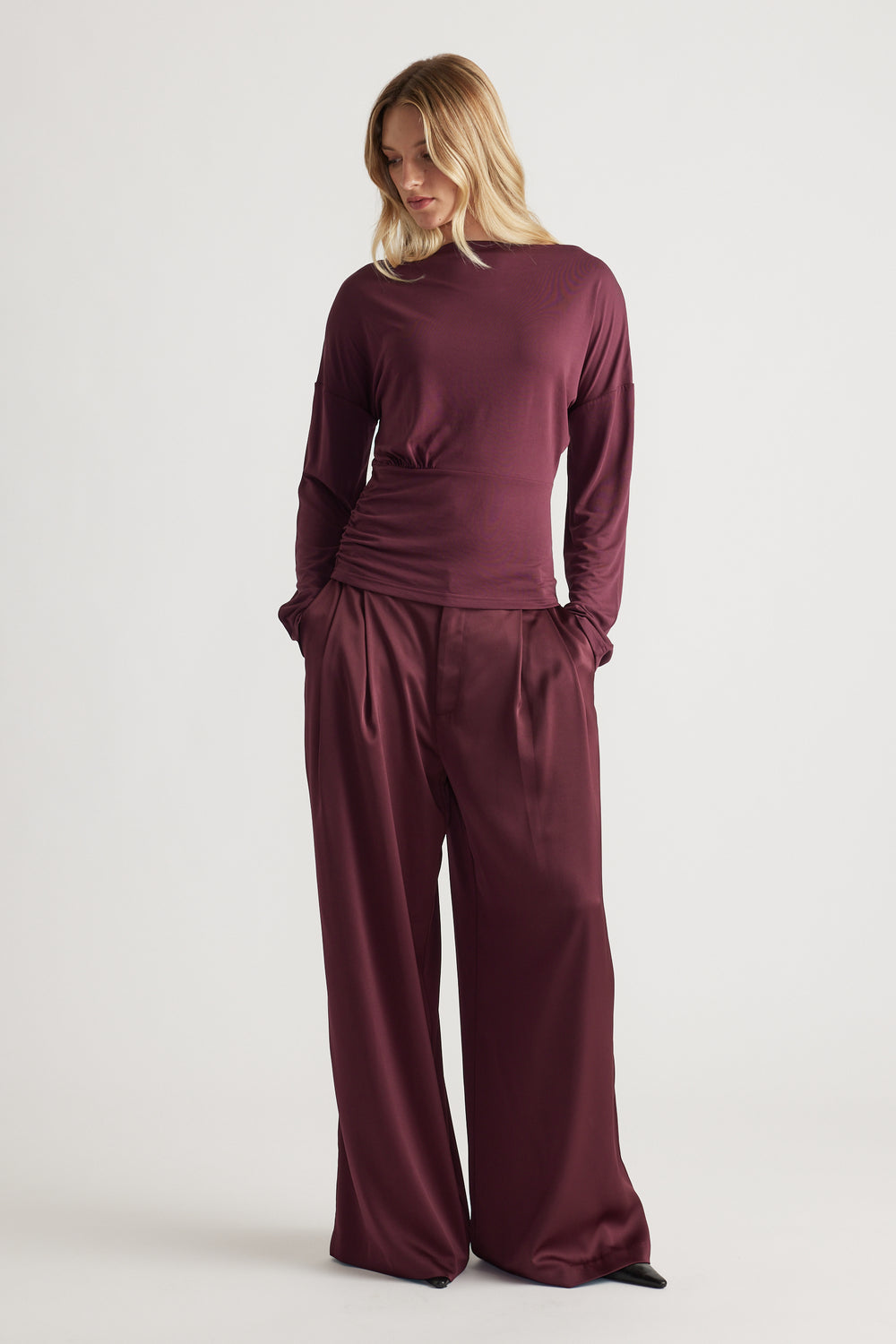 Woman wearing a deep plum cinched long sleeve top paired with matching wide-leg satin pants for a sleek look
