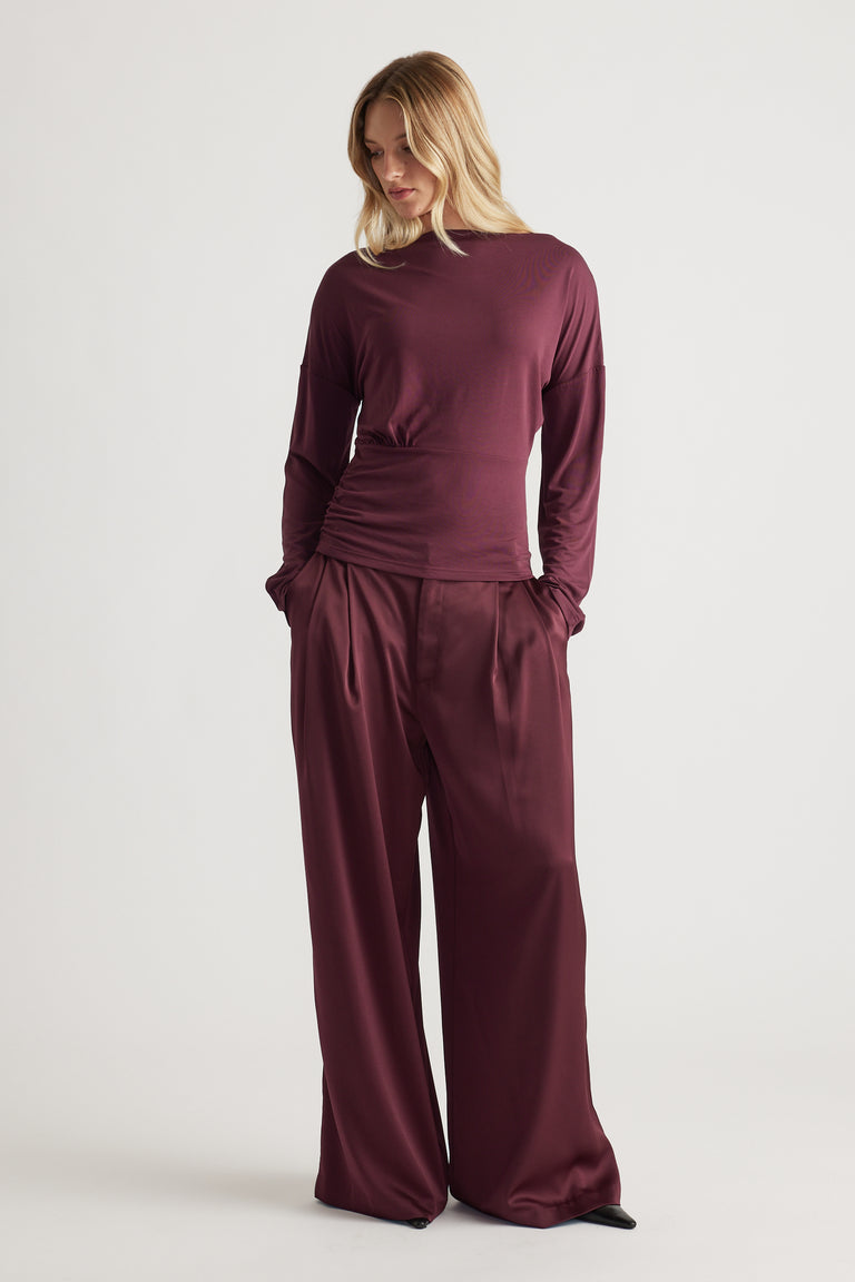 Woman wearing a deep plum cinched long sleeve top paired with matching wide-leg satin pants for a sleek look