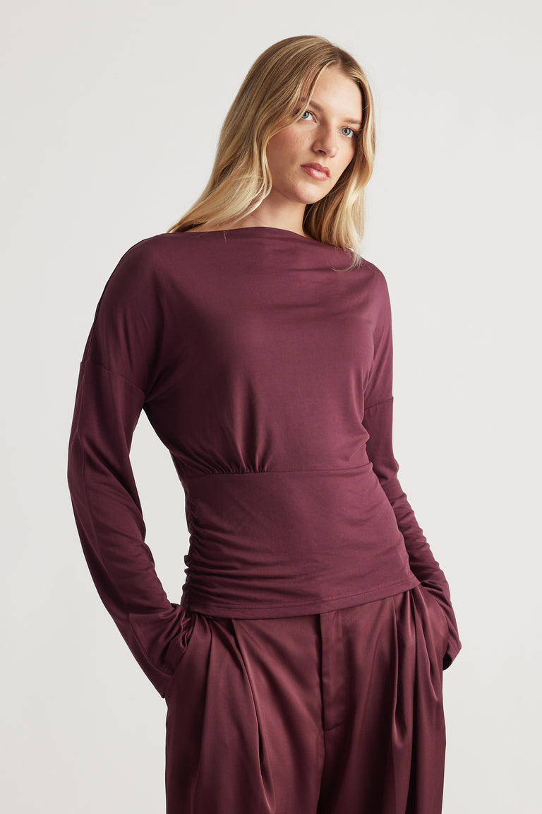 Woman wearing a plum long sleeve top with a cinched waist, styled with relaxed high-waist silky pants for a polished look