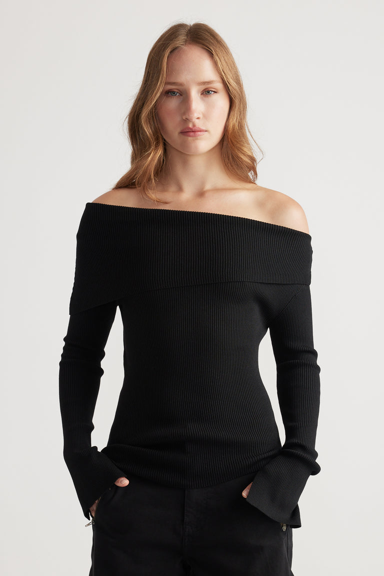 Woman wearing a fitted black off-shoulder ribbed knit top with long flared sleeves paired with black pants