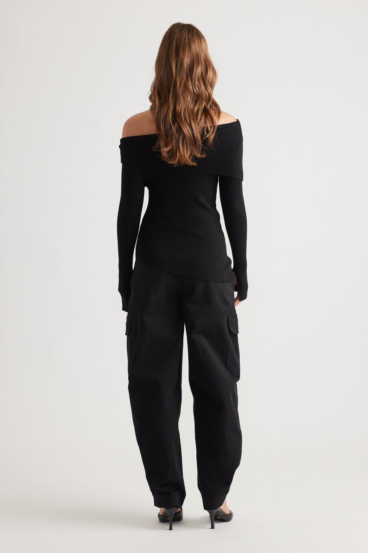 Back view of a fitted black off-shoulder knit top paired with relaxed cargo pants and pointed heels, styled effortlessly.