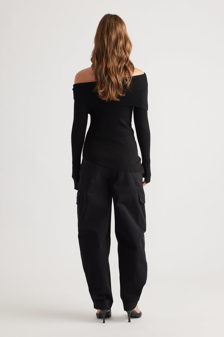 Back view of a fitted black off-shoulder knit top paired with relaxed cargo pants and pointed heels, styled effortlessly.