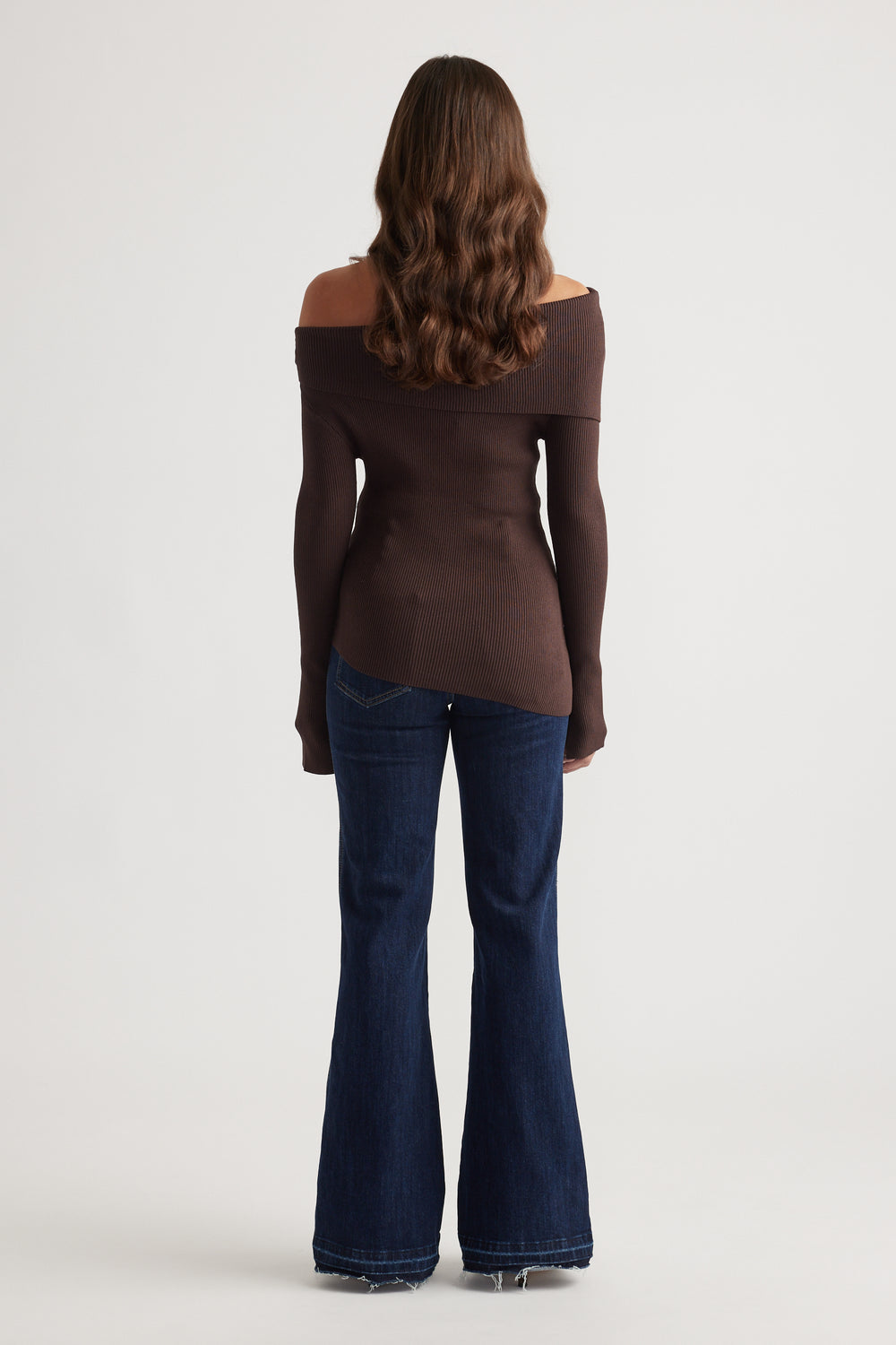 Woman wearing a rich mocha off-shoulder knit top paired with dark flared denim jeans and loose waves hair