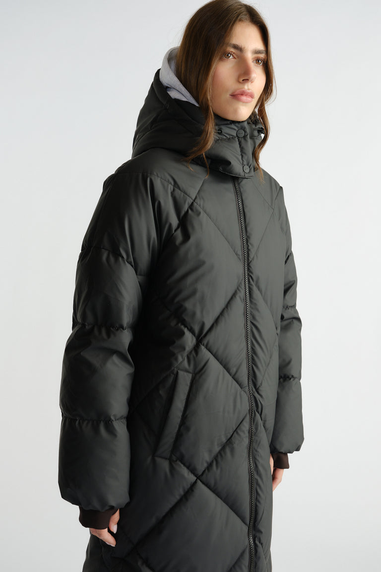 Woman wearing a long black quilted puffer coat with a high collar and hood over a grey inner layer