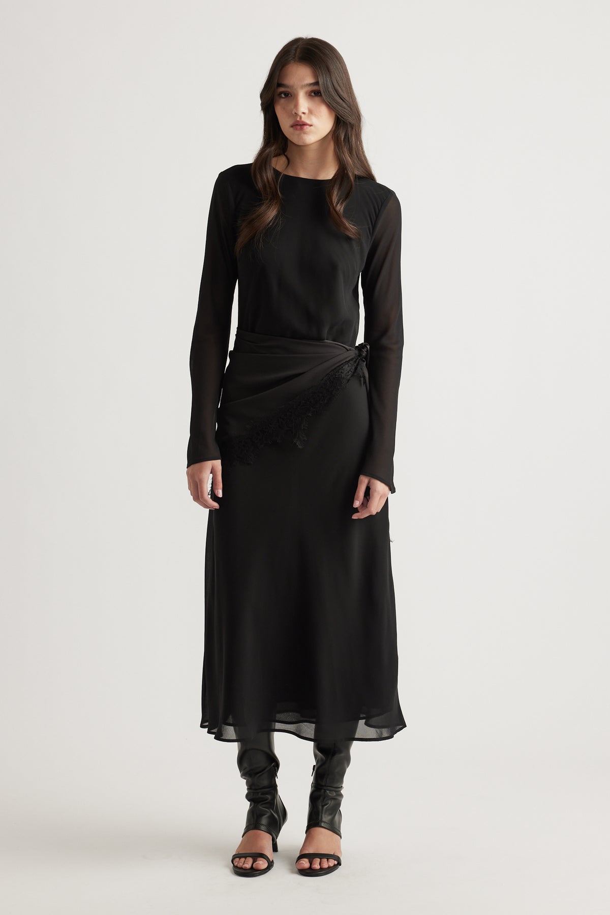 Elegant black maxi dress with sheer long sleeves and a delicate wrap detail, styled with black heeled sandals.