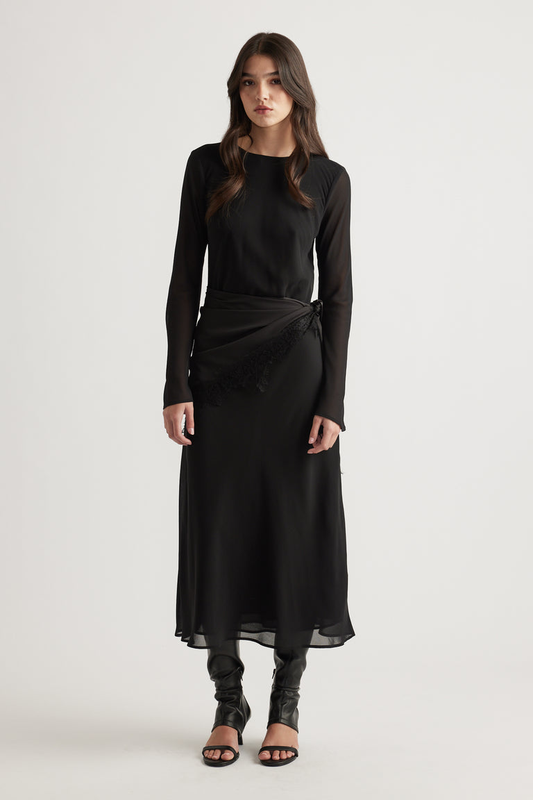 Elegant black maxi dress with sheer long sleeves and a delicate wrap detail, styled with black heeled sandals.