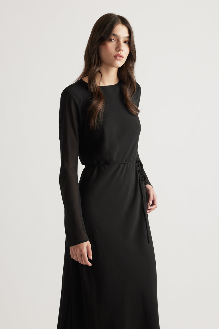Woman wearing a sleek black maxi dress with sheer long sleeves and a waist tie for a refined, modern look