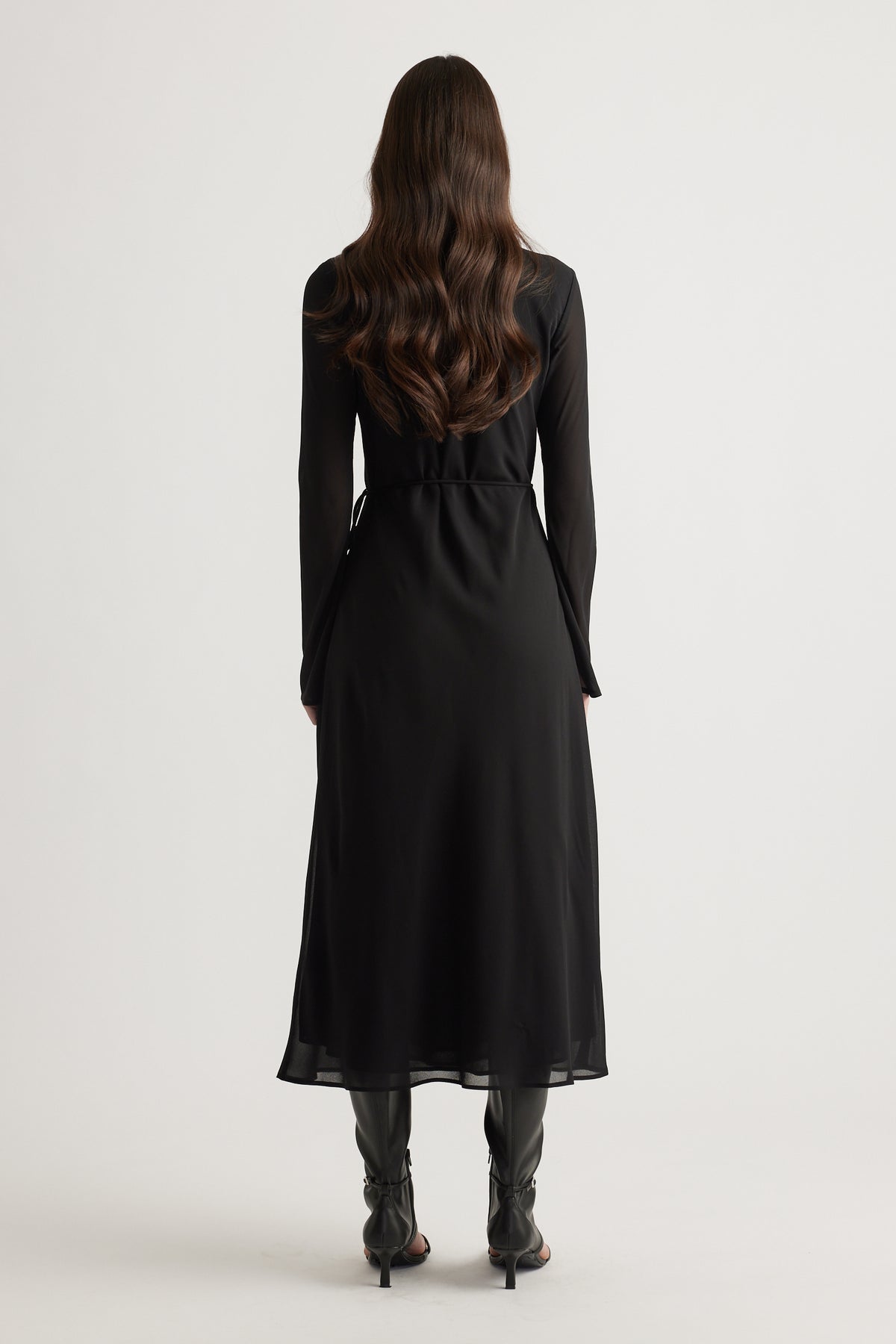 Woman wearing a long black maxi dress with sheer sleeves, styled with black heeled boots for an elegant look