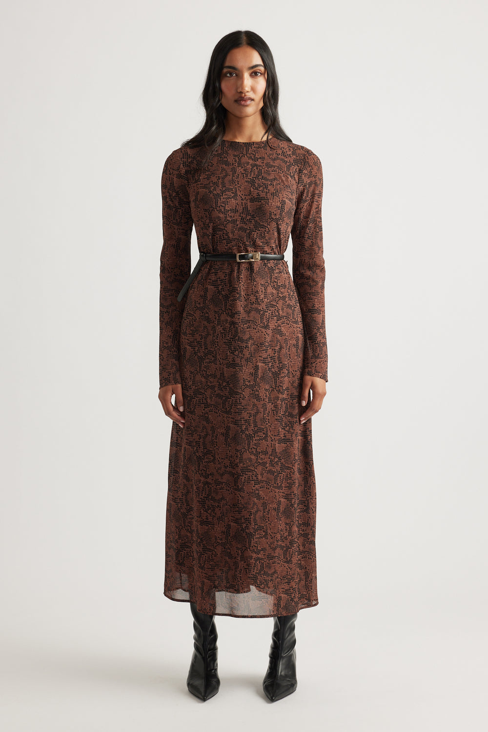Woman wearing a long-sleeve maxi dress with a brown abstract pattern, cinched at the waist with a slim black belt and black boots