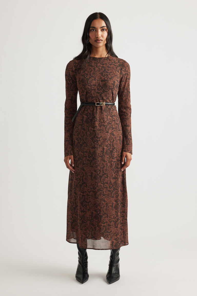 Woman wearing a long-sleeve maxi dress with a brown abstract pattern, cinched at the waist with a slim black belt and black boots