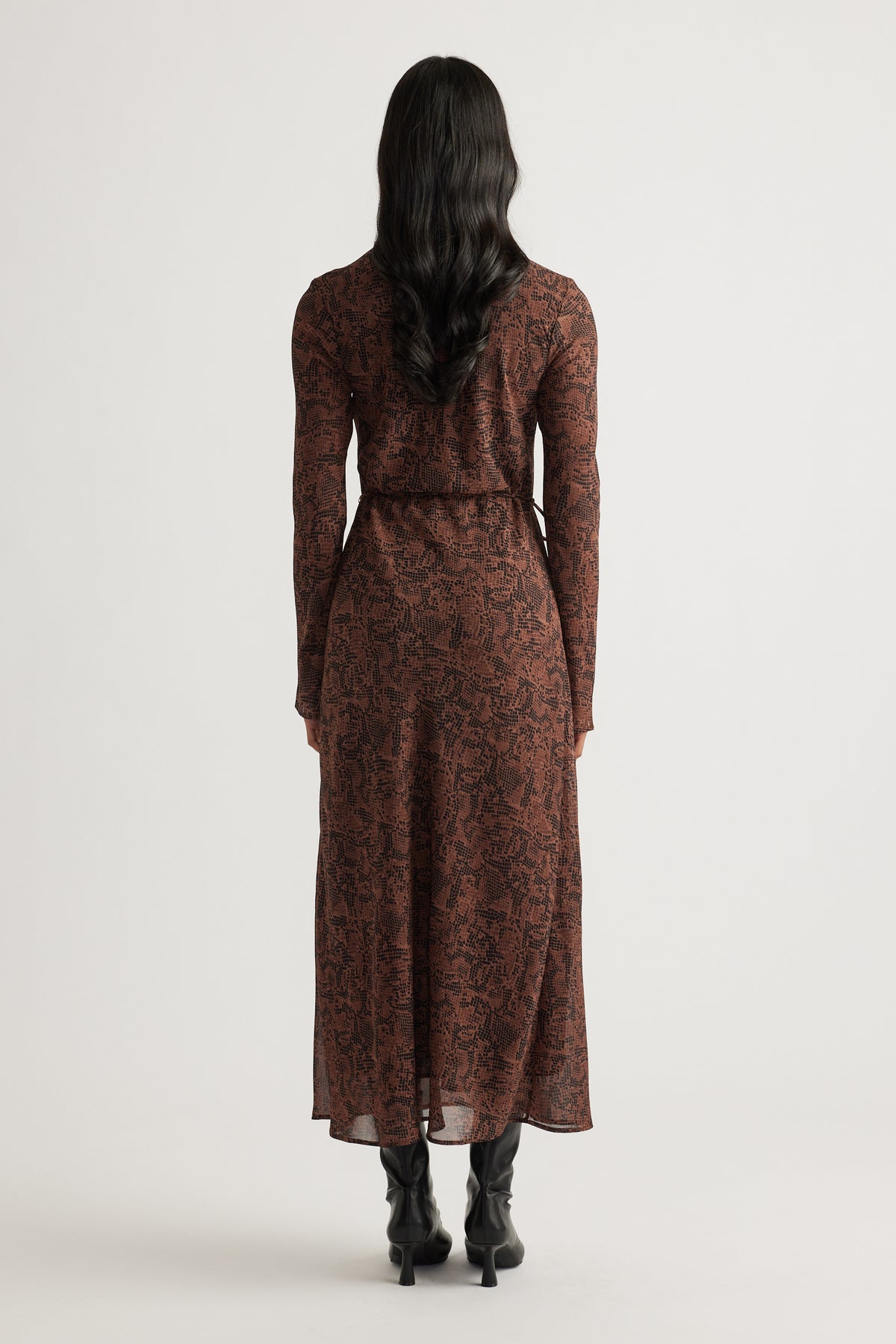 Woman wearing a fitted brown patterned maxi dress with long sleeves, paired with black heeled boots for a sleek look