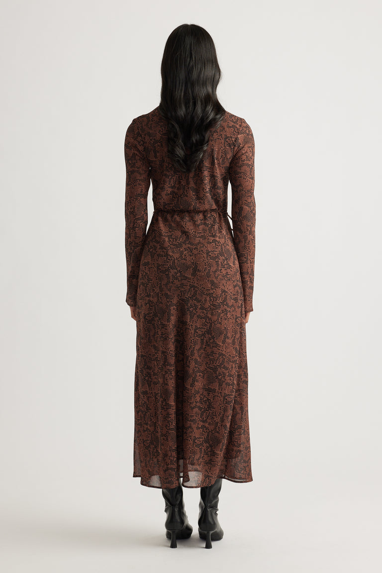 Woman wearing a fitted brown patterned maxi dress with long sleeves, paired with black heeled boots for a sleek look