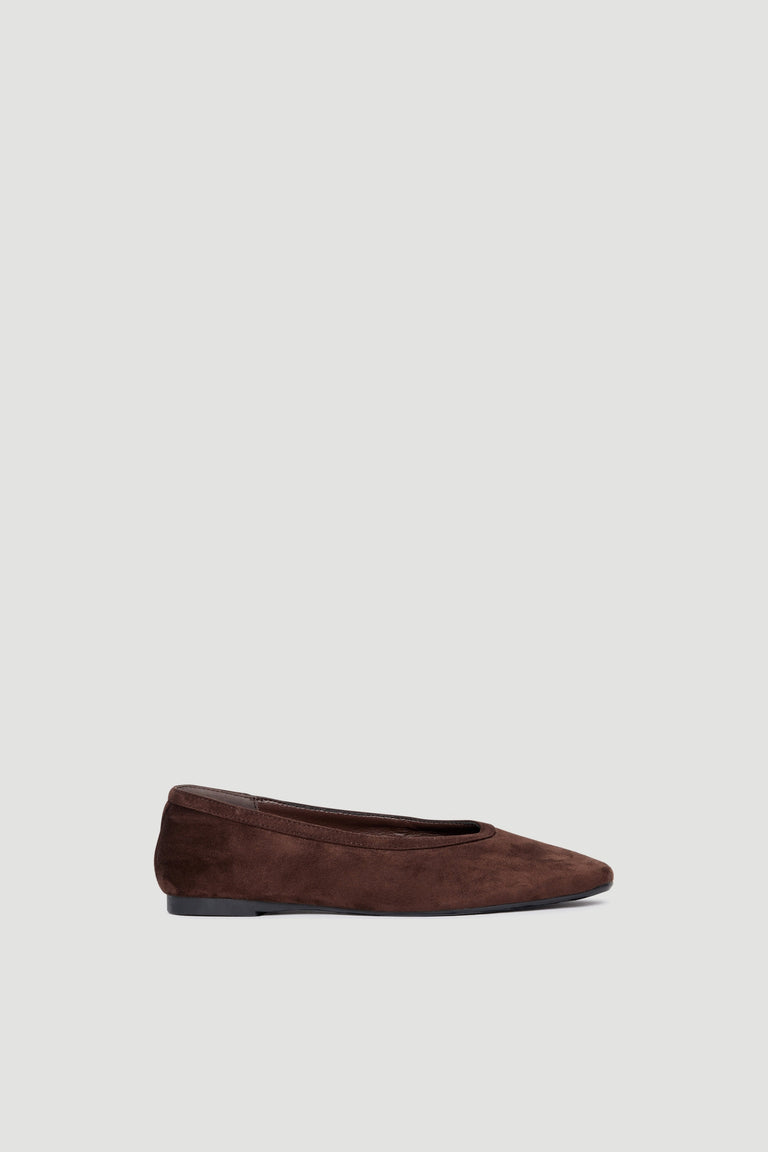 Side view of a chocolate microsuede ballet flat with a rounded toe and low heel on a plain background
