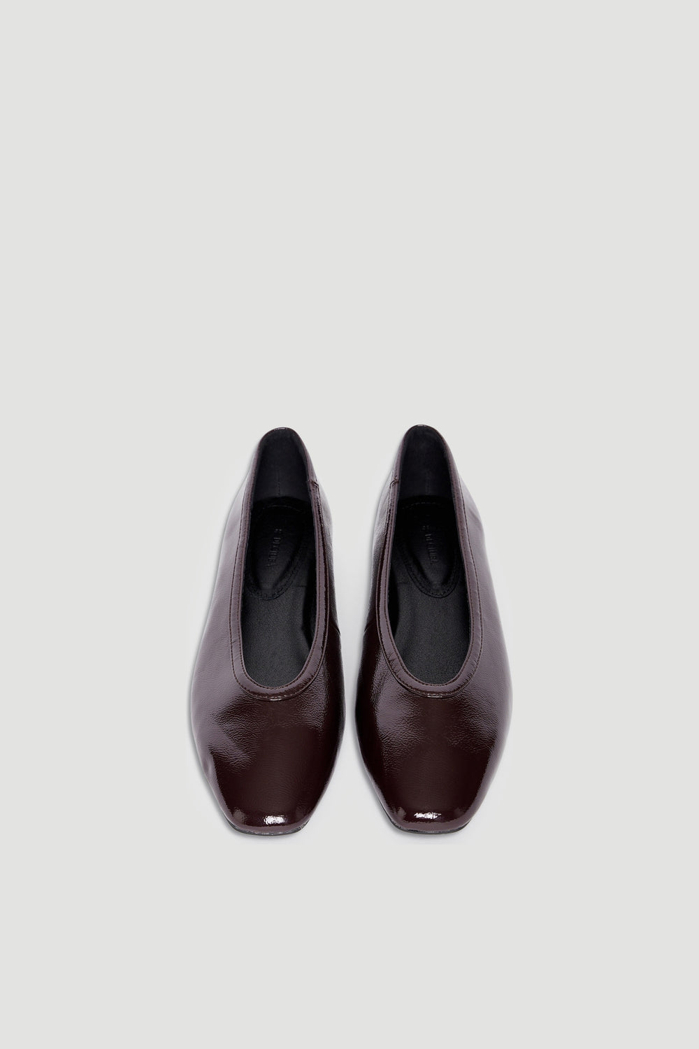 Pair of glossy dark brown square-toe ballet flats with smooth finish on neutral background
