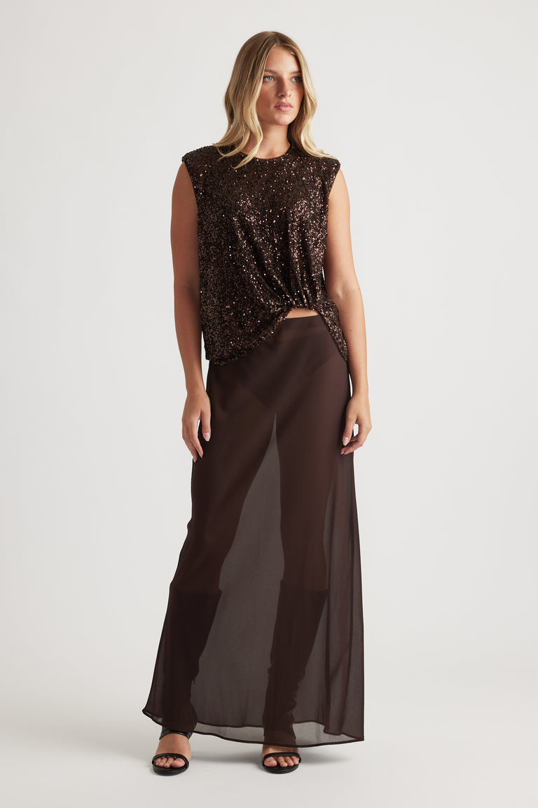 Woman wearing a sleeveless dark brown sequined top paired with sheer wide-leg pants and black sandals on a plain background