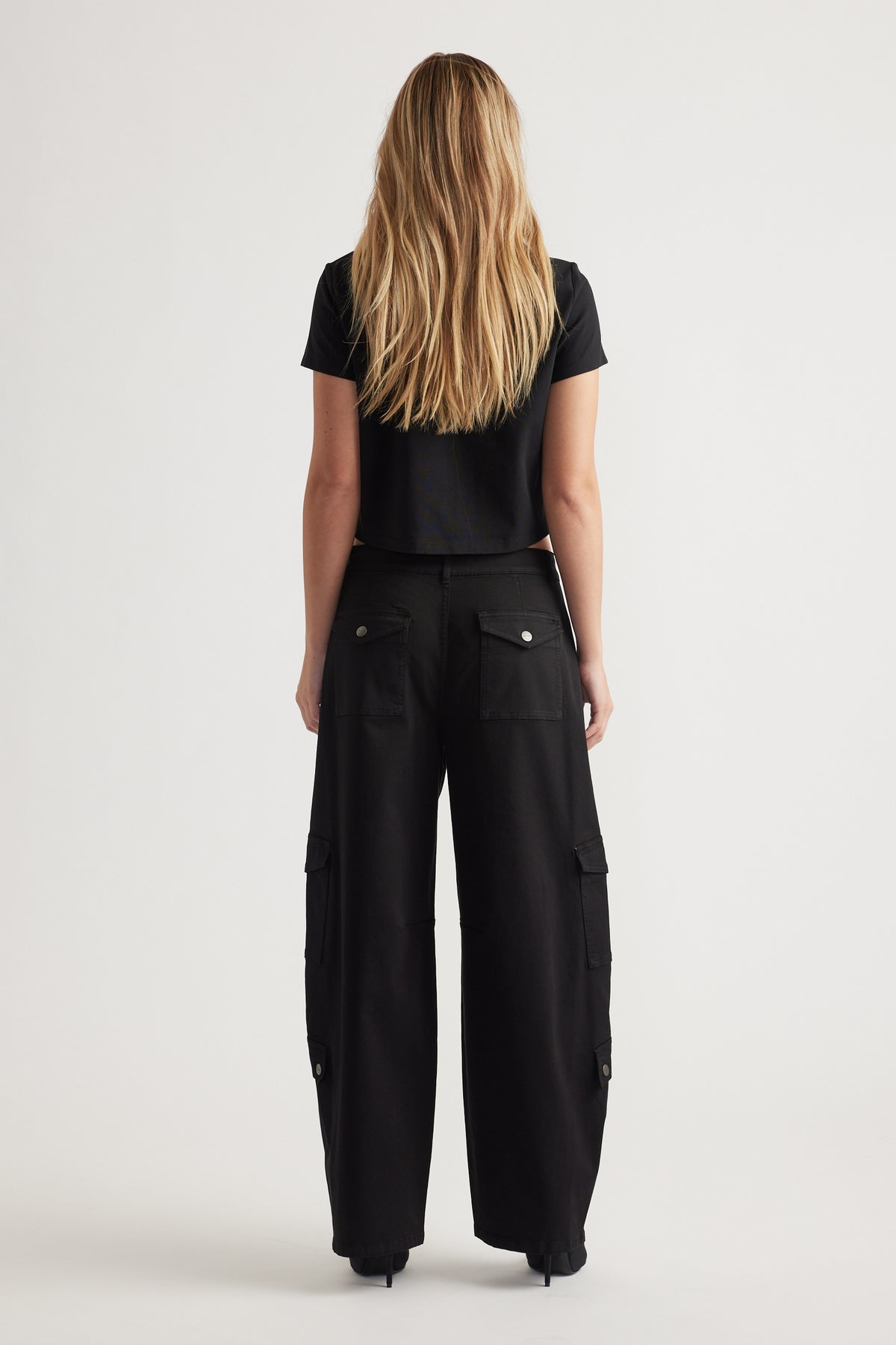 Woman wearing a black cropped tee paired with wide-leg black cargo pants featuring flap pockets, back view.