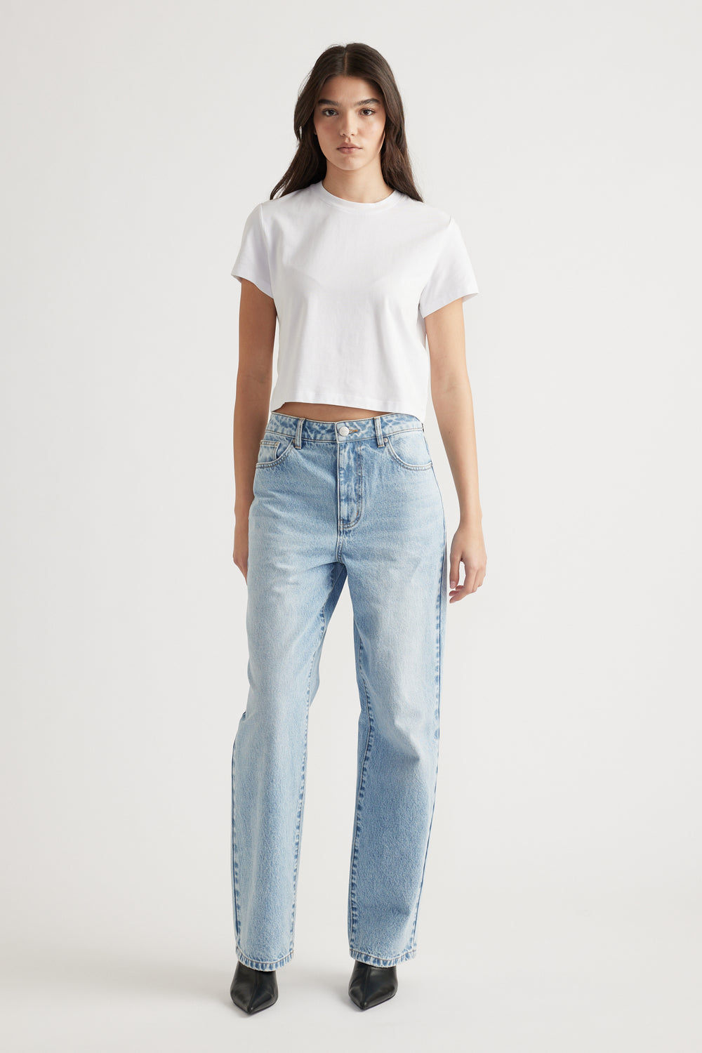 Woman wearing a white cropped tee paired with high-rise light blue straight-leg jeans and black pointed boots.