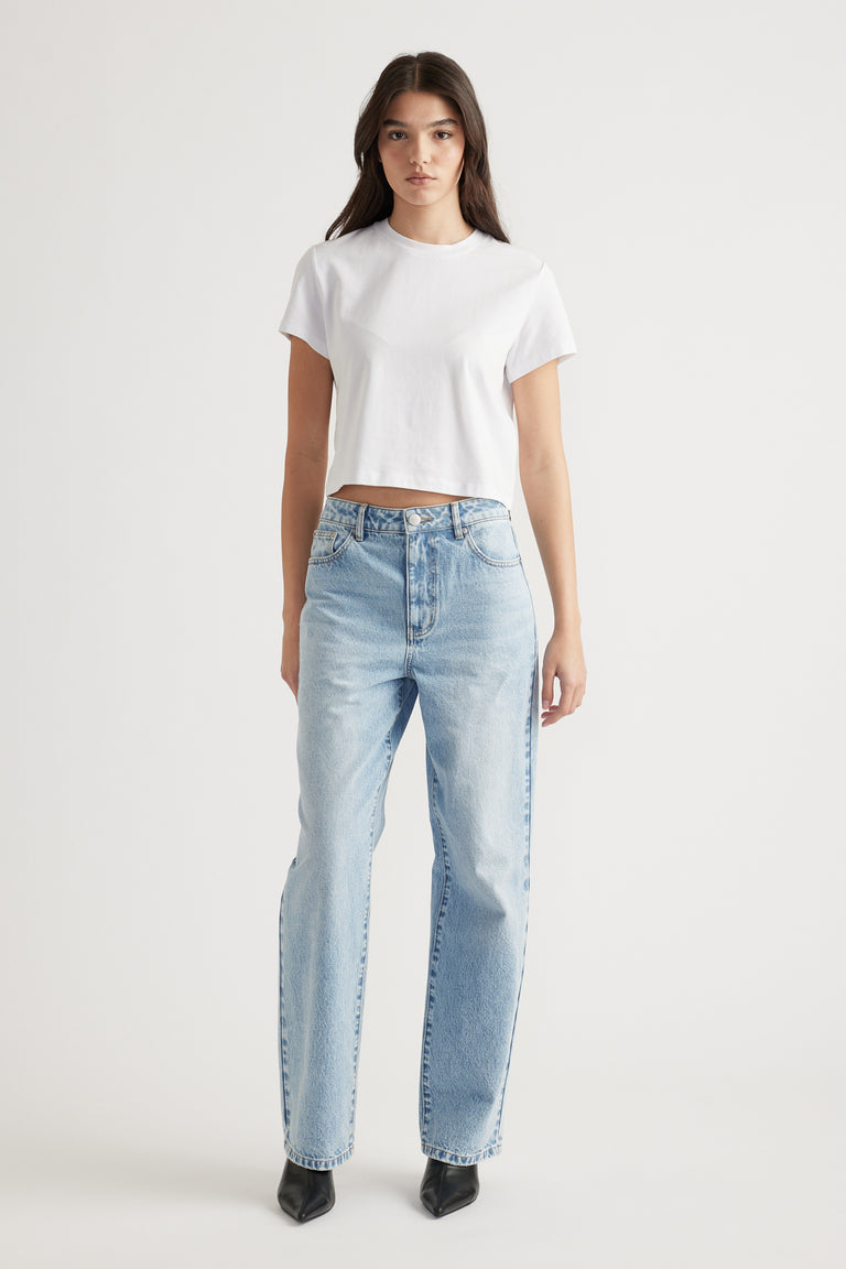 Woman wearing a white cropped tee paired with high-rise light blue straight-leg jeans and black pointed boots.