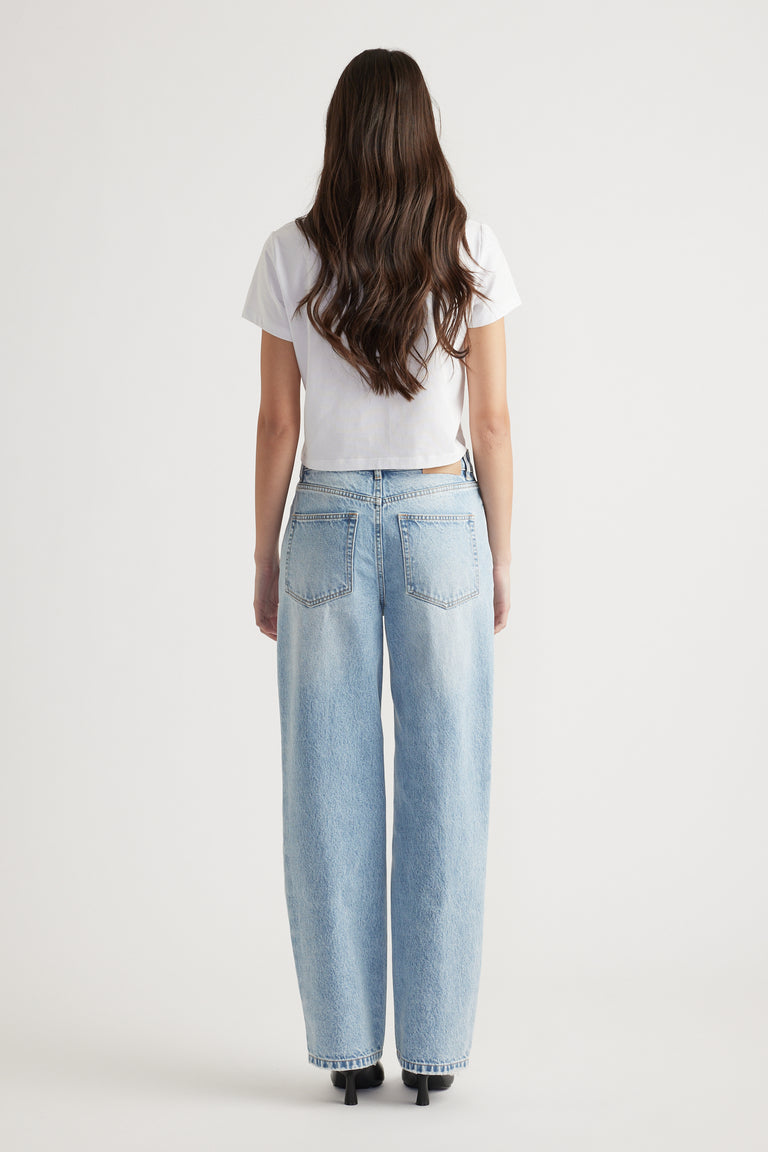 Woman wearing a white cropped tee paired with high-rise, wide-leg light blue denim jeans and black heeled shoes.