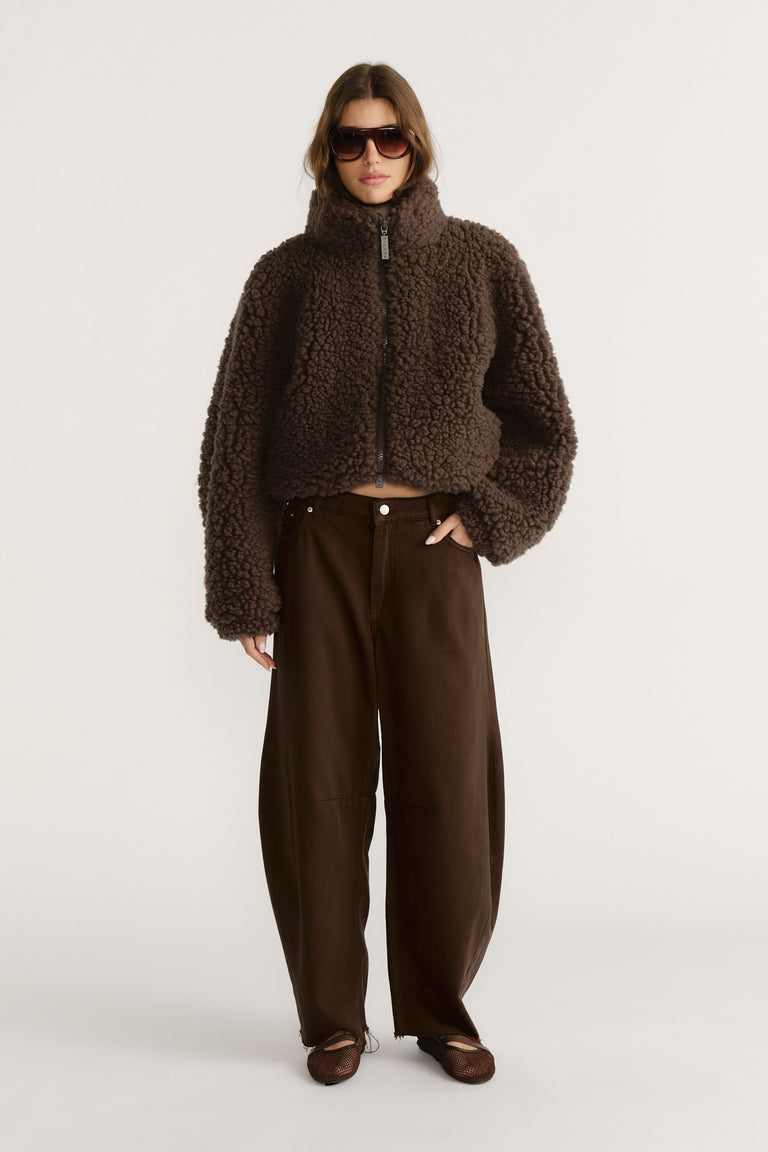 Woman wearing a cropped brown textured jacket with wide-leg dark brown pants and brown pointed flats